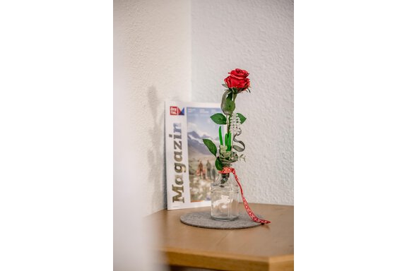 A red rose in a glass vase is sitting on a table. In the background lies a magazine with the title "Magazine." - Apart Wiesengrund - Sölden