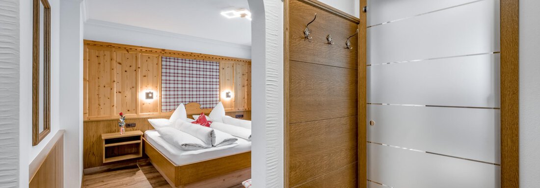 A cozy hotel room with wooden paneling and a bed. The entrance is bright and welcoming. - Apart Wiesengrund - Sölden