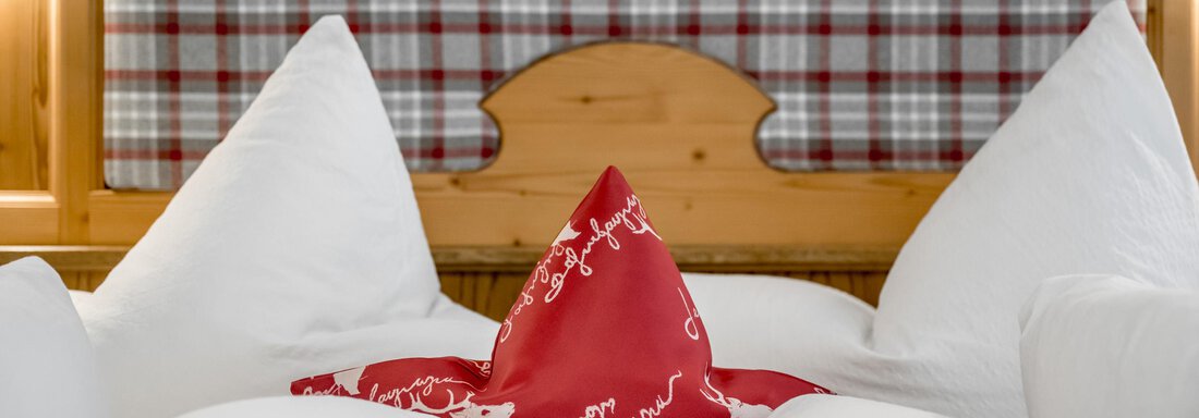 A cozy bed with white pillows and a red star-patterned pillow. In the background, a checkered wooden headboard can be seen. - Apart Wiesengrund - Sölden