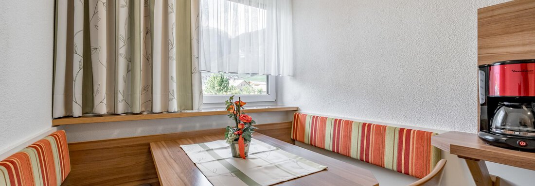 A cozy dining area with a wooden table and colorful benches. A window lets in plenty of natural light and a coffee pot is ready. - Apart Wiesengrund - Sölden