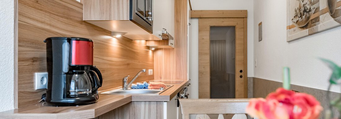 A modern kitchen with wooden details, a cooktop, and a coffee machine. In the foreground, there is a table with flowers. - Apart Wiesengrund - Sölden