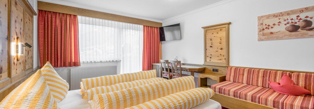 A cozy hotel room with a double bed and striped pillows. There is a small dining area as well as a sofa and decorative elements on the walls. - Apart Wiesengrund - Sölden