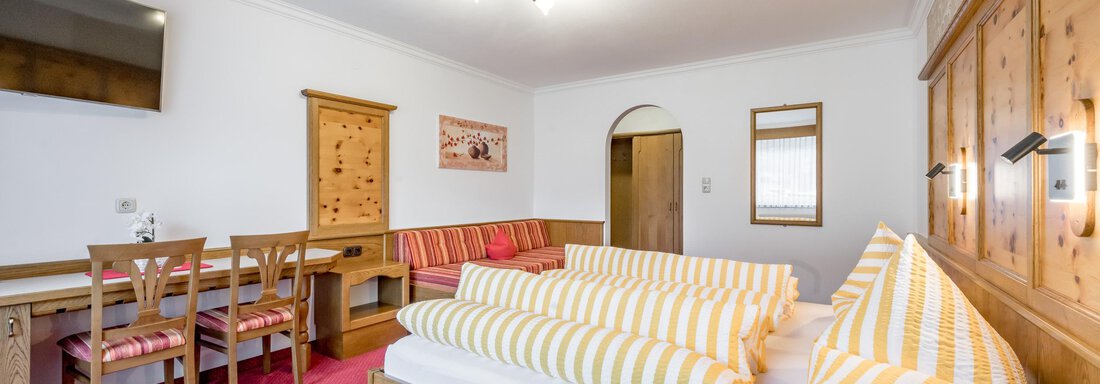 A cozy room with a large bed and striped pillows. There is a dining area with a table and chairs as well as decorative wooden furniture. - Apart Wiesengrund - Sölden