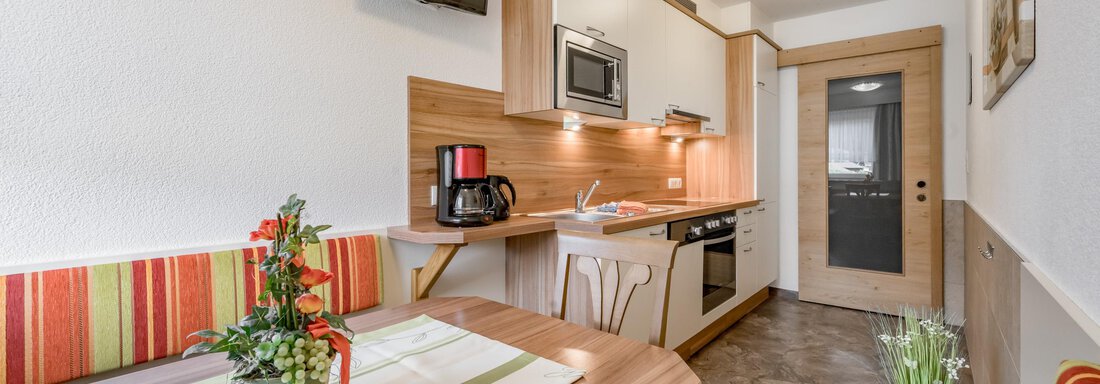 A modern kitchenette with wooden cladding and a small dining area. The room is bright and cheerfully designed. - Apart Wiesengrund - Sölden