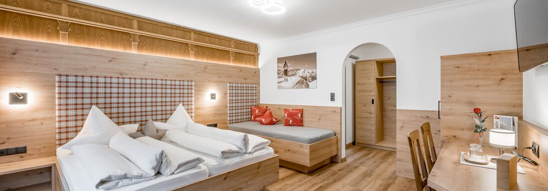 A modern hotel room with wooden furniture and two beds. There is a seating area with a table, a chair, and a small decoration. - Apart Wiesengrund - Sölden