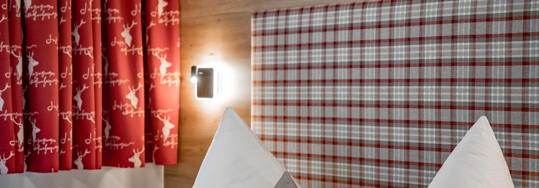 A cozy bedroom with white pillows and a checkered headboard. Curtains in bright red with a pattern create an inviting atmosphere. - Apart Wiesengrund - Sölden