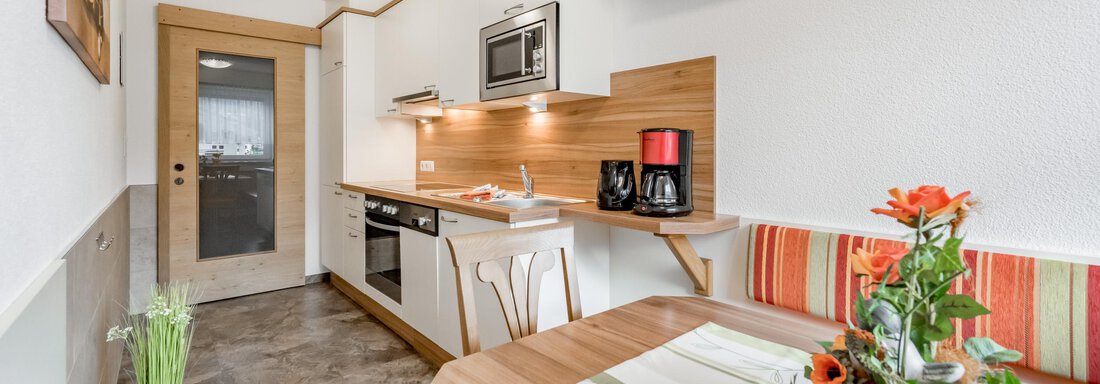 A modern kitchen with wooden details and a cozy eating area. A flower vase and a colorful arrangement are on the table. - Apart Wiesengrund - Sölden
