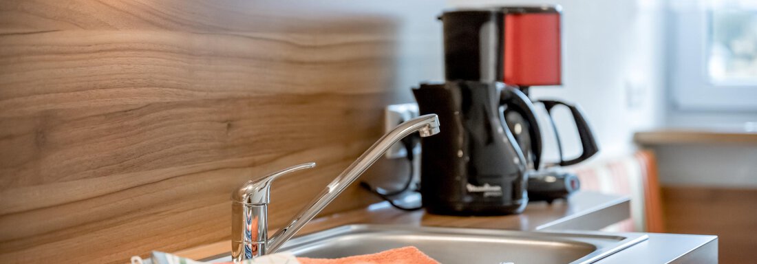 A modern kitchen corner with a sink and kitchen appliances. On the countertop, there is a dish towel and an orange cloth. - Apart Wiesengrund - Sölden