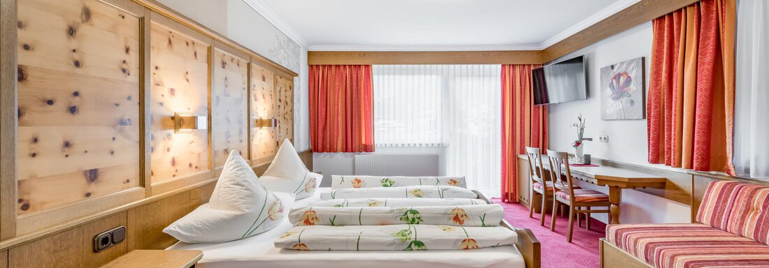 A cozy hotel room with three beds and a large window. The decor is modern and inviting, with red curtains and wooden details. - Apart Wiesengrund - Sölden