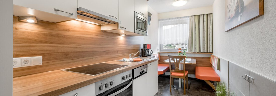 Kitchen A modern kitchen with white cabinets and a wooden countertop. There is a small dining area with red chairs and a window that lets in daylight. - Apart Wiesengrund - Sölden
