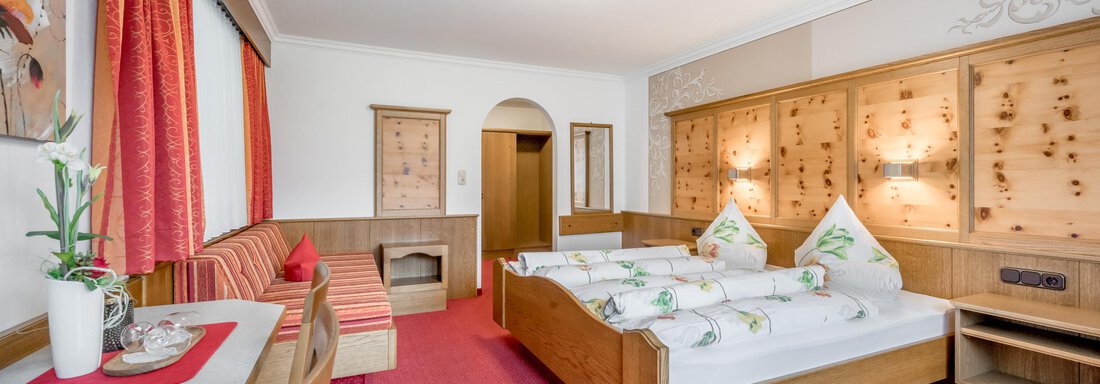 A cozy hotel room with a double bed and wooden paneling. The decor is modern and inviting, with red curtains and a seating area. - Apart Wiesengrund - Sölden