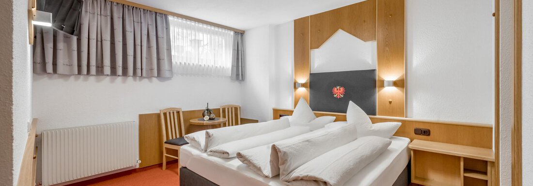 A cozy hotel room with a large bed and elegant wooden furniture. There are windows with curtains and warm light for an inviting atmosphere. - Apart Wiesengrund - Sölden