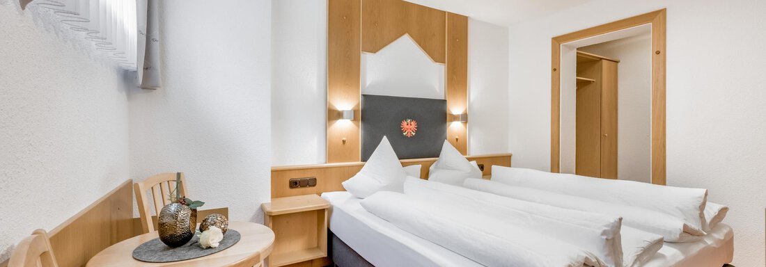 A cozy room with two single beds and a small table. The walls are light and the floor is covered with orange carpet. - Apart Wiesengrund - Sölden