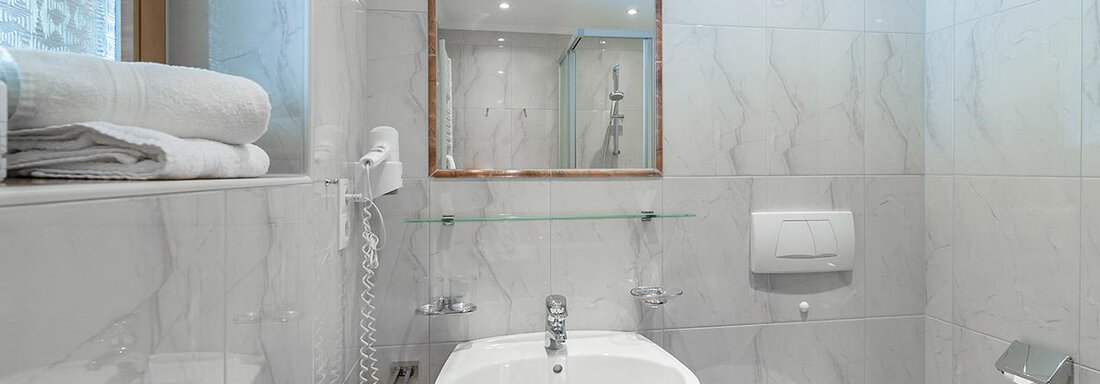 A modern bathroom with bright tiles and a large mirror. It includes a sink, a toilet, and fresh towels. - Apart Wiesengrund - Sölden