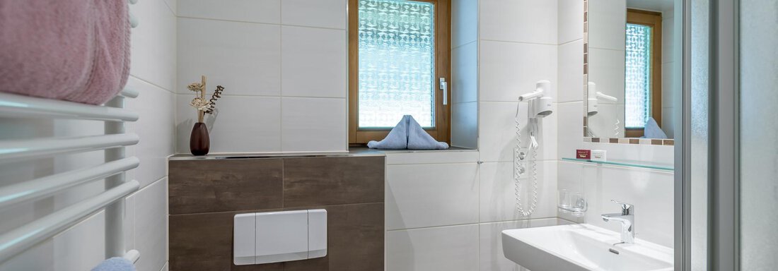 A modern bathroom with bright tiles and a window. There is a sink, a shower, and towels in soft colors. - Apart Wiesengrund - Sölden
