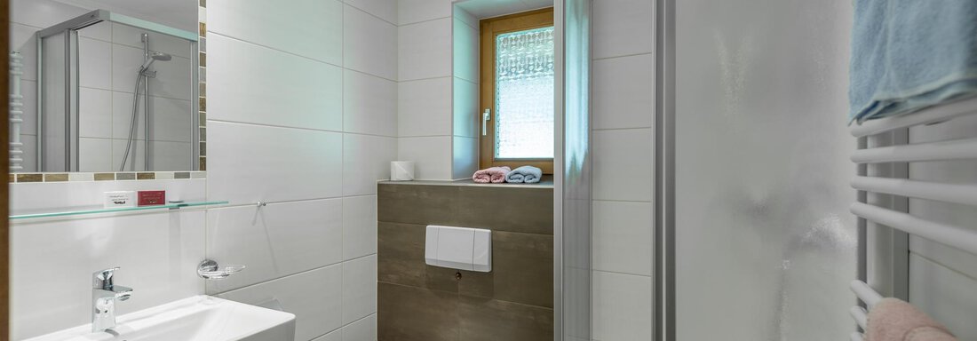A modern bathroom with shower, sink, and toilet. Bright tiles and a window with an outside view create a friendly atmosphere. - Apart Wiesengrund - Sölden