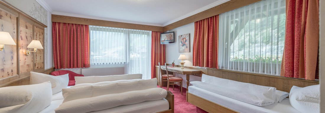 A cozy hotel room with two beds and a table. The large windows let in plenty of daylight and the walls are decorated in warm colors. - Apart Wiesengrund - Sölden