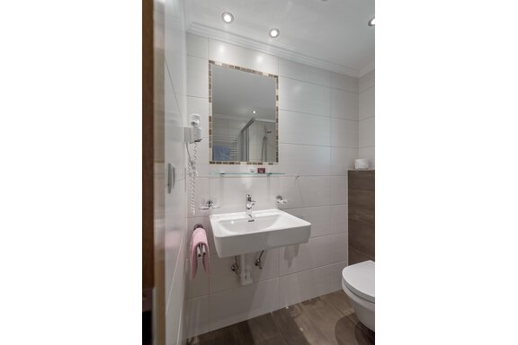 A modern bathroom with a white sink and a large mirror. The walls are light-tiled and there is a toilet in the corner. - Apart Wiesengrund - Sölden