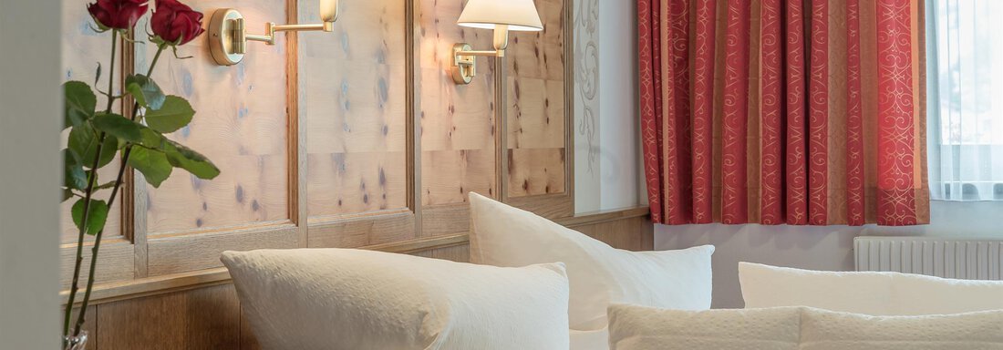 A cozy bedroom with wood paneling and modern fixtures. Fresh roses are on the nightstand, and the beds are outfitted with large, white pillows. - Apart Wiesengrund - Sölden