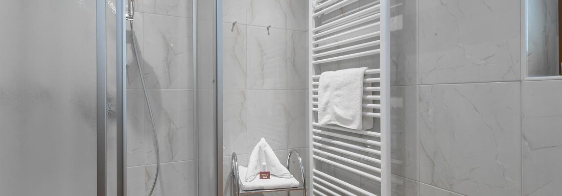 A modern bathroom with a shower and gray tiles. Towels are neatly arranged on a towel warmer and a rolling cart. - Apart Wiesengrund - Sölden
