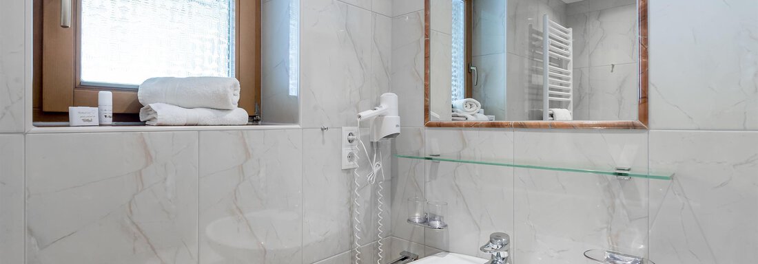 A modern bathroom with bright tiles and a sink. There is a window and fresh towels on a shelf. - Apart Wiesengrund - Sölden