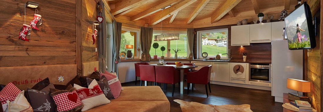 Ein gemütliches Wohn-Esszimmer mit Holzdecke und modernen Möbeln. Die große Fensterfront bietet einen Blick auf die saftige Wiese draußen. - Alpen Diamond Top 100 | 300 | 700 - Sölden