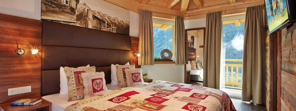 Ein gemütliches Schlafzimmer mit einem großen Bett und einer bunten Decke. Es gibt Holzdetails und einen Balkon mit Aussicht auf die Berge. - Alpen Diamond Top 100 | 300 | 700 - Sölden