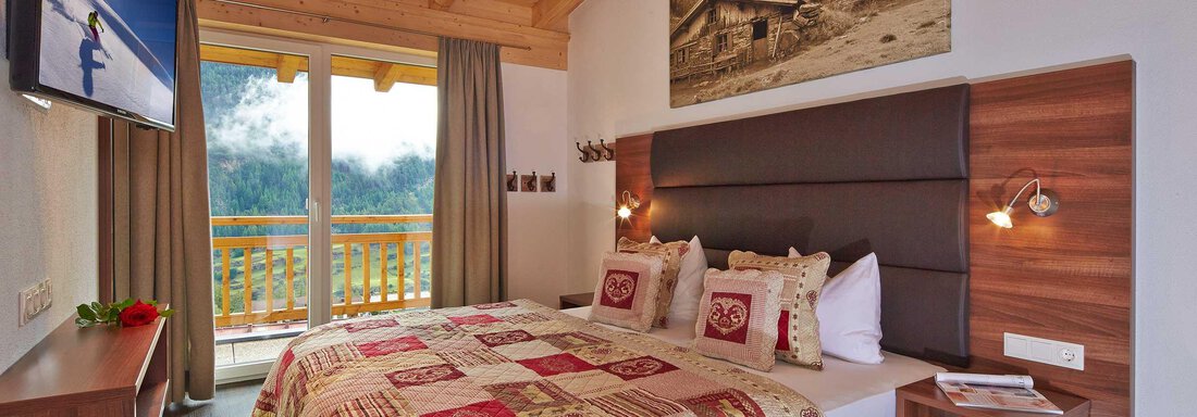 Ein gemütliches Schlafzimmer mit Holzwänden und einem großen Fenster. Das Bett ist mit einer bunten Decke dekoriert und es gibt einen Fernseher an der Wand. - Alpen Diamond Top 100 | 300 | 700 - Sölden