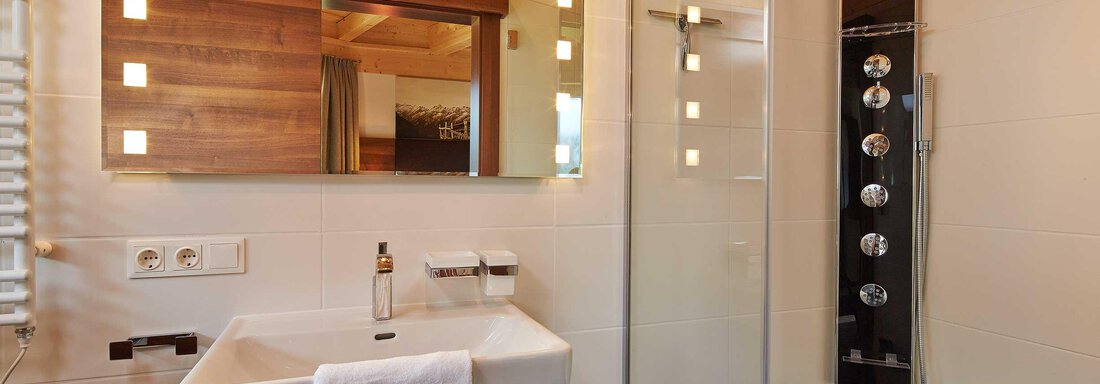 Ein modernes Badezimmer mit einer Dusche, einem eleganten Waschbecken und einem großen Spiegel. Die Wände sind hell und mit Holzdetails gestaltet. - Alpen Diamond Top 100 | 300 | 700 - Sölden