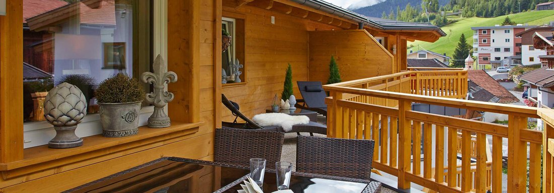 Eine gemütliche Terrasse mit einem Tisch und Stühlen aus Rattan. Im Hintergrund sind die Berge und ein schönes Dorf zu sehen. - Alpen Diamond Top 100 | 300 | 700 - Sölden