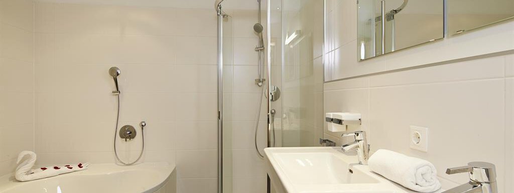 Ein modernes Badezimmer mit einer Dusche und einer Badewanne. Helle Fliesen und elegante Sanitäreinrichtungen sorgen für eine einladende Atmosphäre. - Alpen Diamond Top 100 | 300 | 700 - Sölden