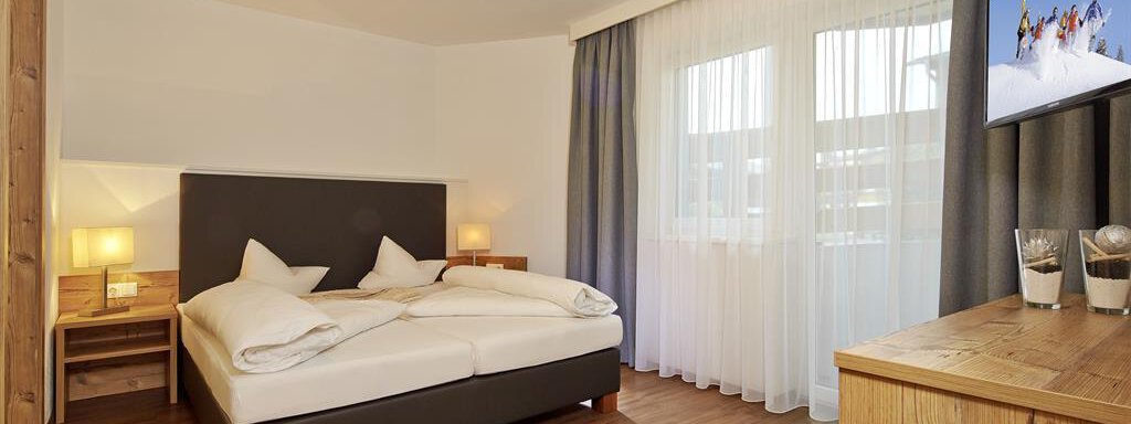 Ein modernes Schlafzimmer mit einem Doppelbett, Holz- und Textil-Elementen. Große Fenster lassen viel Licht hinein und sorgen für eine helle Atmosphäre. - Alpen Diamond Top 100 | 300 | 700 - Sölden