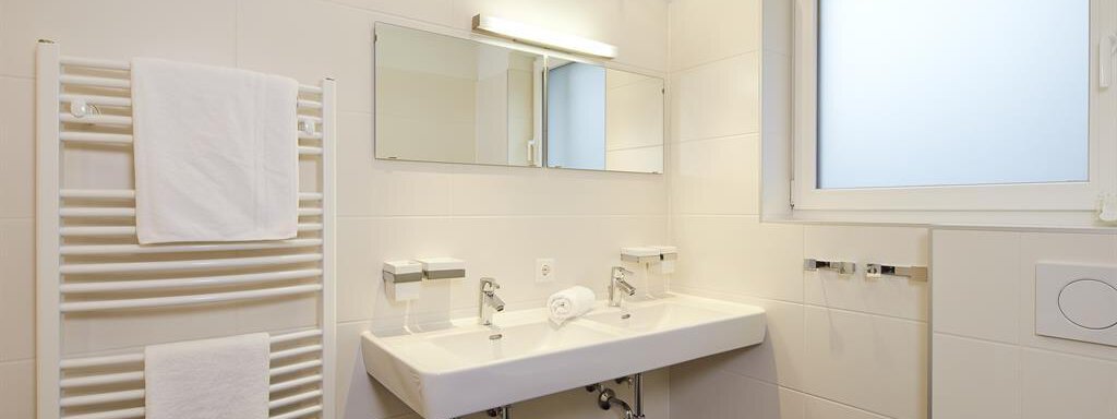 Ein modernes Badezimmer mit einem doppelt Waschbecken und einem großen Spiegel. Weiße Wände und ein Handtuch-Heizkörper verleihen dem Raum eine helle, saubere Atmosphäre. - Alpen Diamond Top 100 | 300 | 700 - Sölden