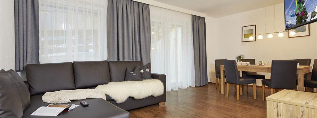 Ein modernes Wohnzimmer mit einer gemütlichen Couch und einem Holztisch. Große Fenster lassen viel Licht herein und die Einrichtung ist schlicht und elegant. - Alpen Diamond Top 100 | 300 | 700 - Sölden