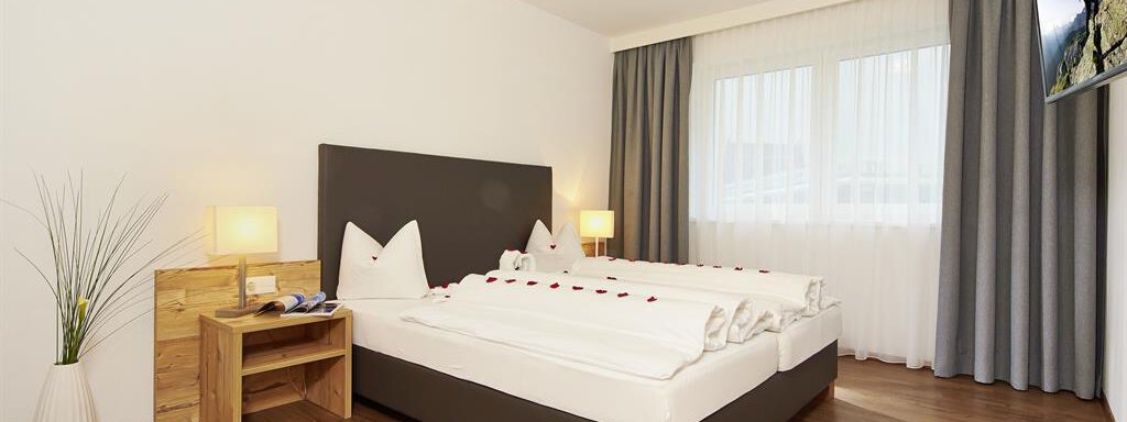 Ein modernes Schlafzimmer mit einem großen Bett und Holzfußboden. Große Fenster lassen viel Licht herein, und dekorative Elemente sorgen für eine gemütliche Atmosphäre. - Alpen Diamond Top 100 | 300 | 700 - Sölden