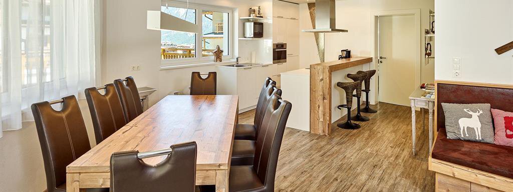 Ein modernes Esszimmer mit einem großen Holztisch und eleganten Stühlen. Die Küche ist offen und hell mit einer angenehmen Atmosphäre. - Alpen Diamond Top 100 | 300 | 700 - Sölden