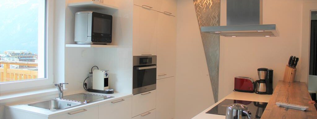 Eine moderne Küche mit weißen Schränken und einer großen Fensterfront. Es gibt eine Kochstelle, moderne Geräte und Holzarbeitsflächen. - Alpen Diamond Top 100 | 300 | 700 - Sölden