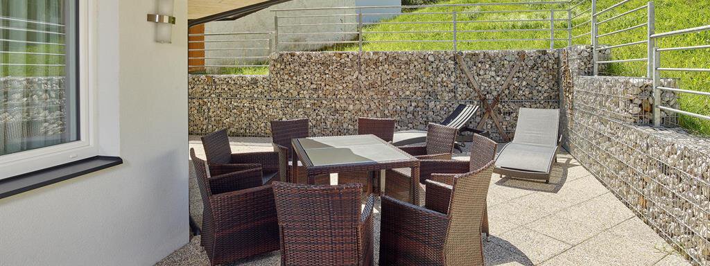 Eine gemütliche Terrasse mit einem Tisch und Stühlen aus Rattan, umgeben von grünem Gras und Bergen. Der perfekte Ort zum Entspannen im Freien. - Alpen Diamond Top 100 | 300 | 700 - Sölden