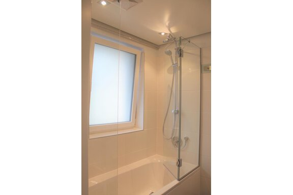 Ein modernes Badezimmer mit einer Badewanne und einer Duschkabine. Das große Fenster lässt viel natürliches Licht herein. - Alpen Diamond Top 100 | 300 | 700 - Sölden