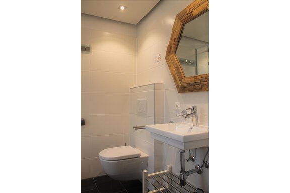 Ein modernes Badezimmer mit einer weißen Toilette und einem eleganten Waschbecken. Der runde Holzrahmen des Spiegels verleiht dem Raum eine warme Atmosphäre. - Alpen Diamond Top 100 | 300 | 700 - Sölden