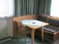 A cozy dining area with a wooden chair and a corner bench. The table is decorated with a tablecloth and a bowl. - Appartement Almhof - Sölden