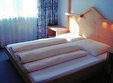 Zimmer A simple bedroom with a wooden bed and several pillows. The window lets in a lot of daylight. - Appartement Almhof - Sölden