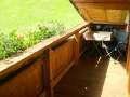 A wooden balcony with a wooden railing and a small table. In the background, a green meadow is visible. - Appartement Almhof - Sölden