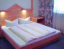 Zimmer A cozy bedroom with a large bed and two pillows. The room has a bright atmosphere with a window and decorative curtains. - Appartement Almhof - Sölden