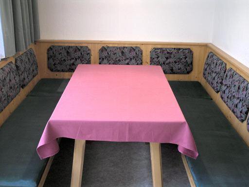 A cozy dining area with a pink tablecloth and benches. The walls are light, and the windows are covered with curtains. - Appartement Almhof - Sölden