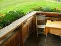 A cozy table with a yellow tablecloth and a white chair on a terrace. In the background, a green garden can be seen. - Appartement Almhof - Sölden
