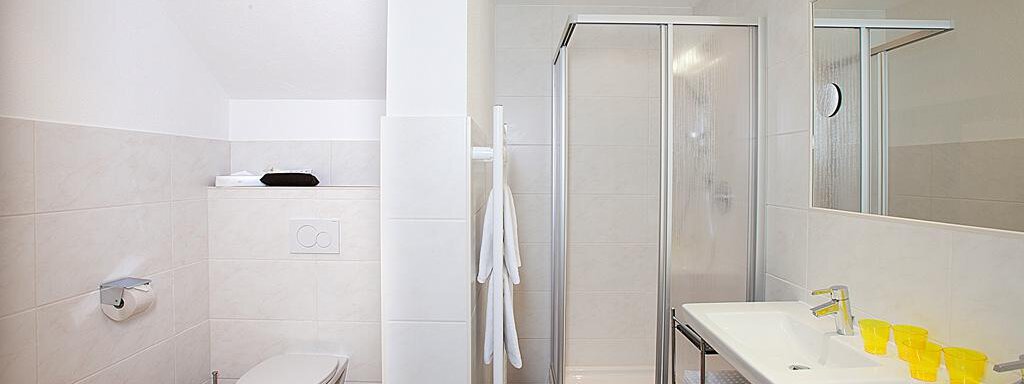 A modern bathroom with a shower and toilet. The washbasin has yellow and transparent towels. - Appartement Alpin - Sölden