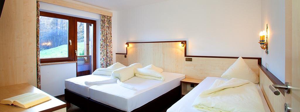 A bright room with two single beds and a small table. Through the window, you can see the outdoor area with plants. - Appartement Alpin - Sölden