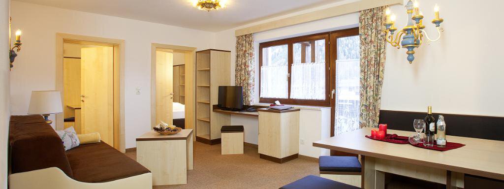 A cozy living room with a comfortable couch and a dining table. Large windows provide plenty of natural light and an inviting atmosphere. - Appartement Alpin - Sölden