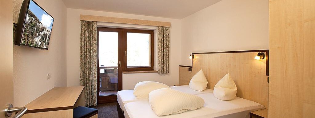 A modern bedroom with two beds and light wood decor. There is a television on the wall and a small desk. - Appartement Alpin - Sölden